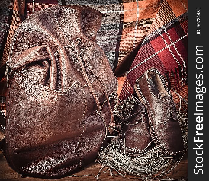 Leather backpack and shoes on the background of wool tartan on the wooden floor. Leather backpack and shoes on the background of wool tartan on the wooden floor