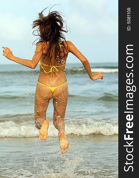 Bikini clad woman jumping in water by sunset