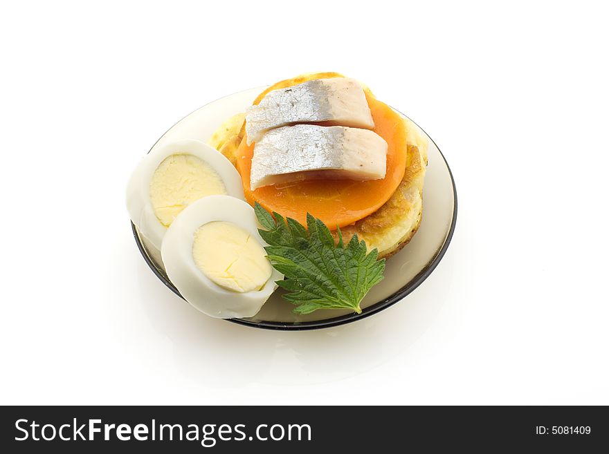 Pickled herring on a plate with boiled egg, carrot slices, pancake and nettle leaf, white background. Pickled herring on a plate with boiled egg, carrot slices, pancake and nettle leaf, white background