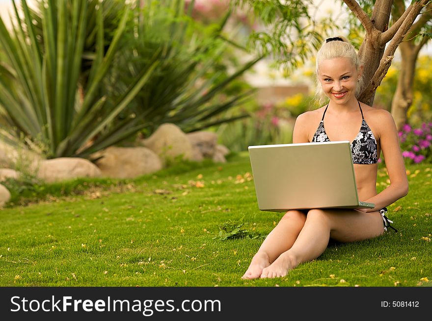 Girl sitting on grass in a garden with a laptop. Girl sitting on grass in a garden with a laptop