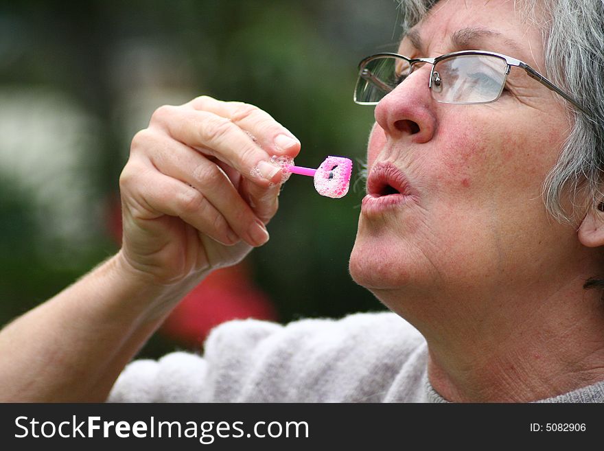 An old woman blowing bubbles like a child. An old woman blowing bubbles like a child