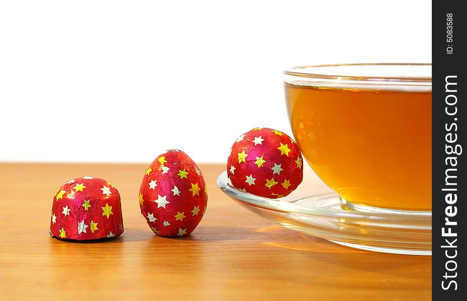 Chocolates in a red wrapper and a cup of tea. Chocolates in a red wrapper and a cup of tea