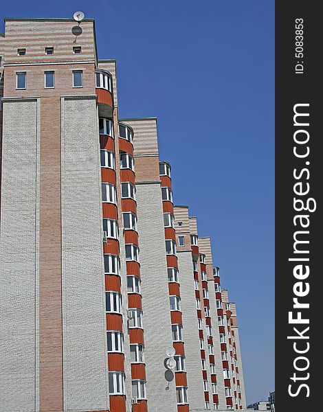 New brick multistoried building with red balconies on a background blue sky, social habitation