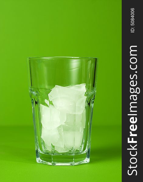 Glass of ice on green background