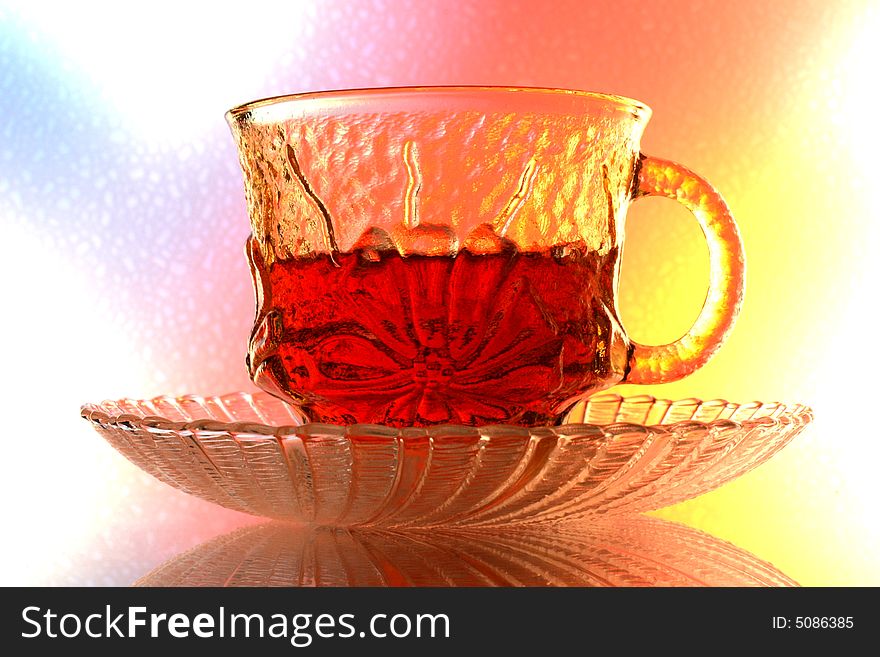 Close-up of glass teacup and saucer  against multi colored abstract background. Close-up of glass teacup and saucer  against multi colored abstract background