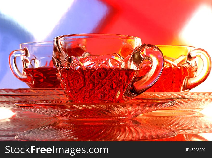 Close-up of glass teacup and saucer against multi colored abstract background. Close-up of glass teacup and saucer against multi colored abstract background