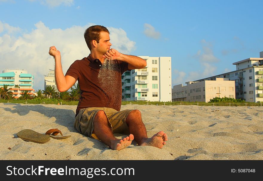 Man tossing sand to the side while sitting on the beach.