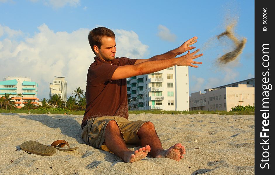 Man tossing sand to the side while sitting on the beach.
