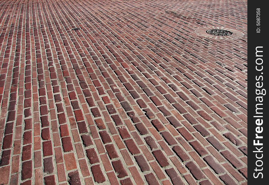 A red brick road with a drain in the upper right corner