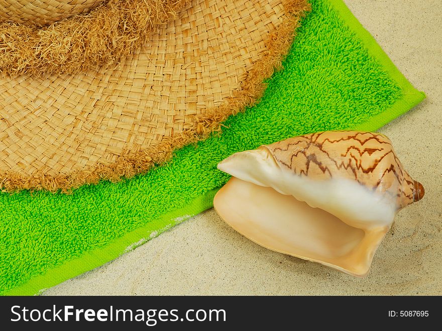 Seashell, straw hat and green towel on the coral sand. Seashell, straw hat and green towel on the coral sand