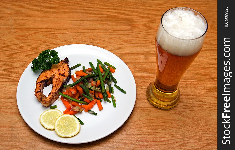 Light beer and fried salmon with vegetables on wooden background. Light beer and fried salmon with vegetables on wooden background