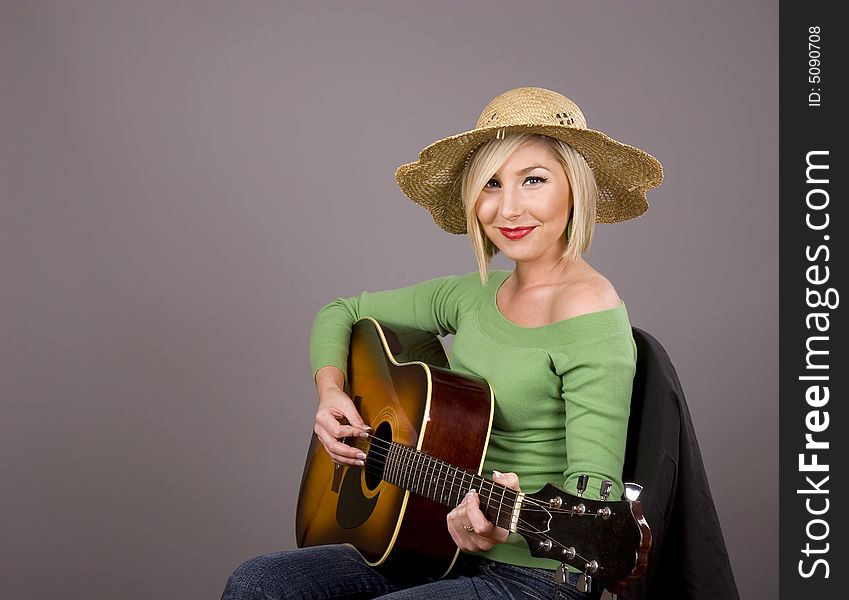 A blonde wearing a green blouse and a straw hat posing with a guitar. A blonde wearing a green blouse and a straw hat posing with a guitar
