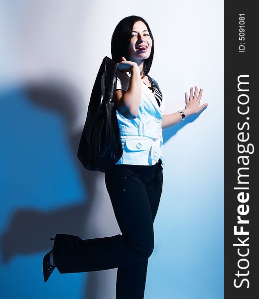 A high-key portrait about a cute trendy girl with black hair who is lighted with blue and she has an attractive look. She is wearing black pants, a white coat and a stylish handbag. A high-key portrait about a cute trendy girl with black hair who is lighted with blue and she has an attractive look. She is wearing black pants, a white coat and a stylish handbag.