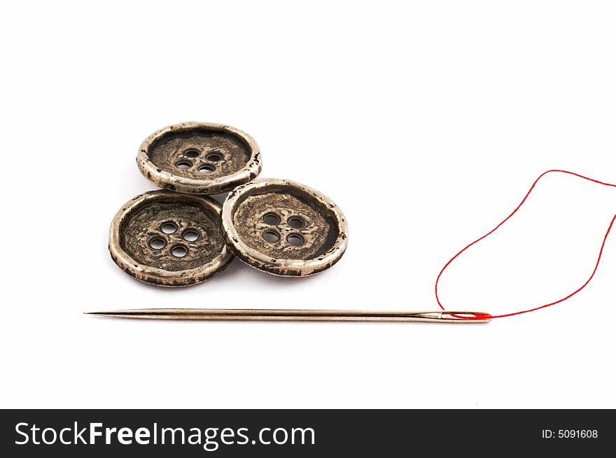 Three metal buttons and needle isolated on white