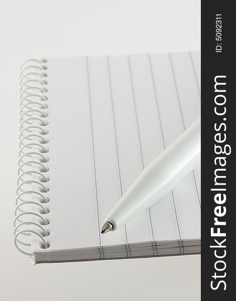 An open spiral bound notebook with lines paper and a white pen