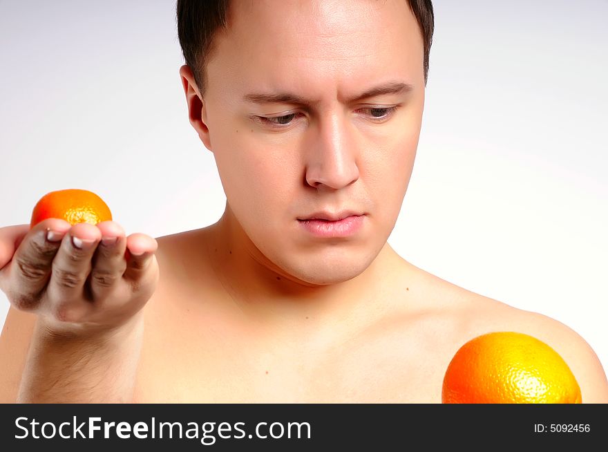 Man with two fresh bright oranges makes a choice. Man with two fresh bright oranges makes a choice