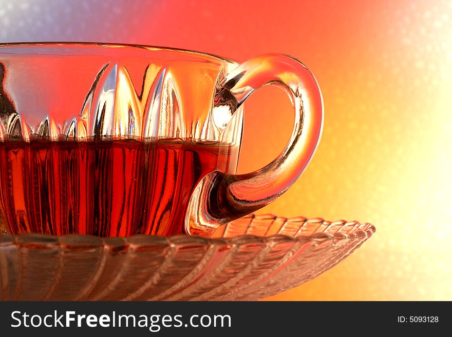 Close-up of glass teacup and saucer against multi colored abstract background. Close-up of glass teacup and saucer against multi colored abstract background