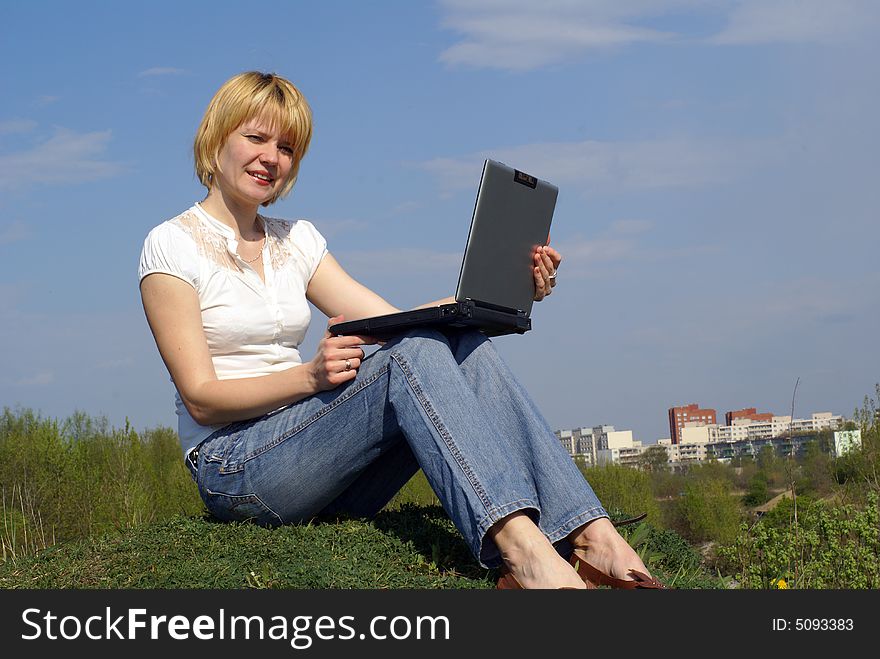 Woman is working with notebook on green grass and blue sky on background