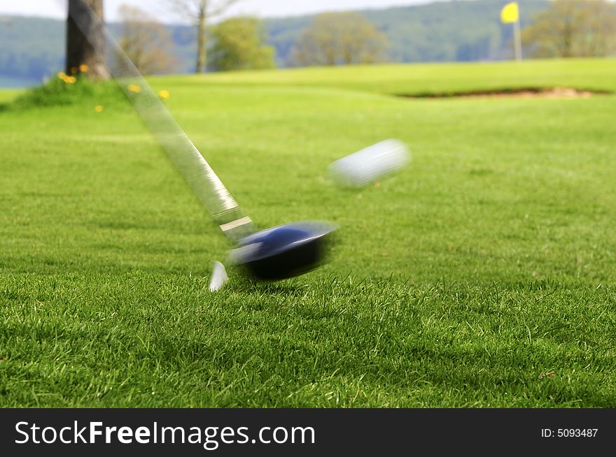 Hitting a white ball from tee with flag and bunker in background. Hitting a white ball from tee with flag and bunker in background