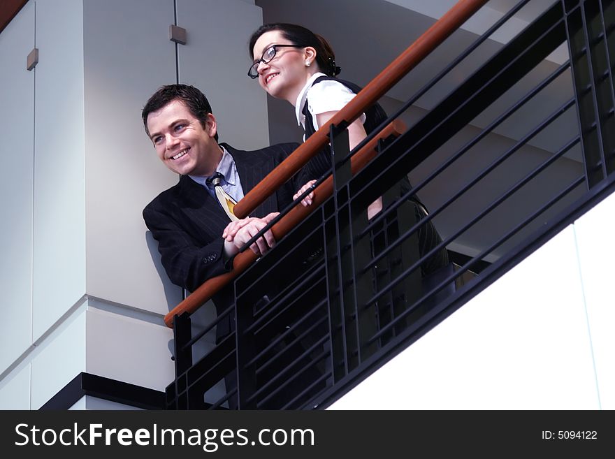 Male and female business colleagues standing by a railing and smiling. Male and female business colleagues standing by a railing and smiling