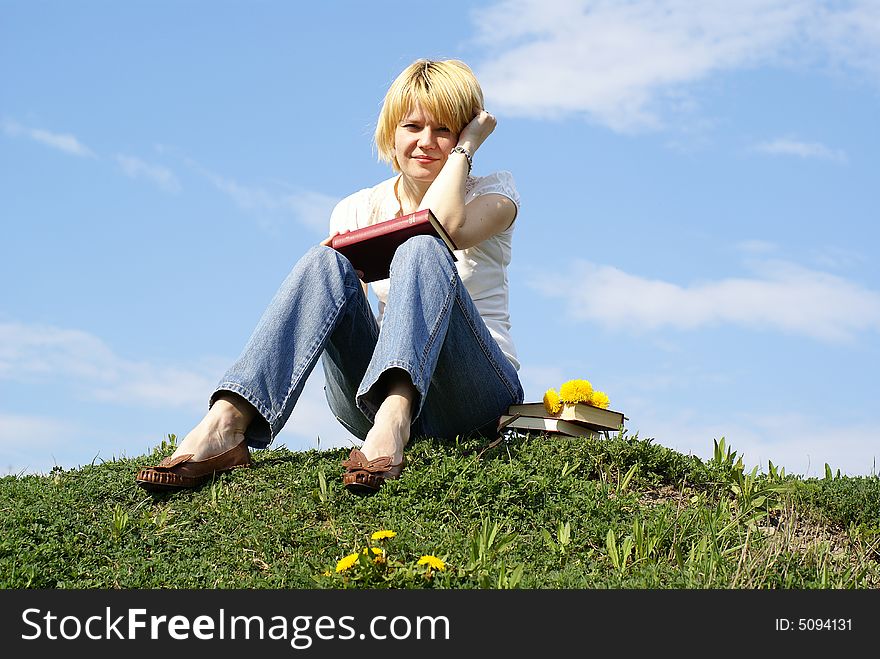 Female student outdoor on green grass with books and blue sky on background