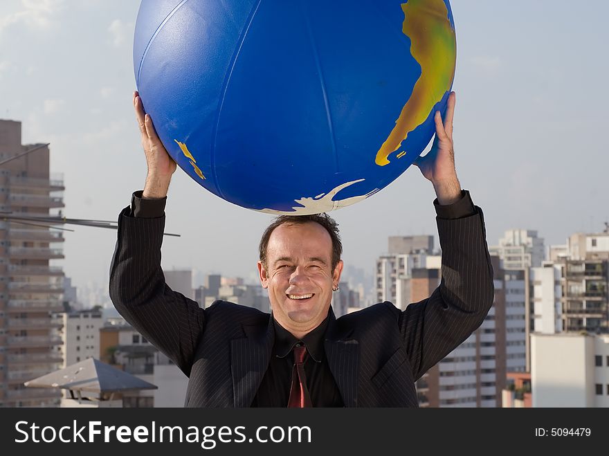 Businessman standing on the roof of a building with the city in the background holding a large globe in one hand. Businessman standing on the roof of a building with the city in the background holding a large globe in one hand.