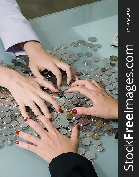 Close-up of two sets of female hands (on either side of a desk) grabbing at a large pile of coins in between them. Close-up of two sets of female hands (on either side of a desk) grabbing at a large pile of coins in between them.