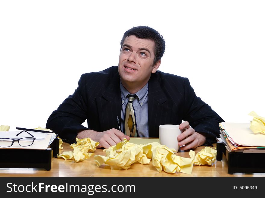 An isolated shot of a businessman sitting at desk, topped with crumpled yellow paper, looking up towards the ceiling/sky, with a bewilered expression. An isolated shot of a businessman sitting at desk, topped with crumpled yellow paper, looking up towards the ceiling/sky, with a bewilered expression.