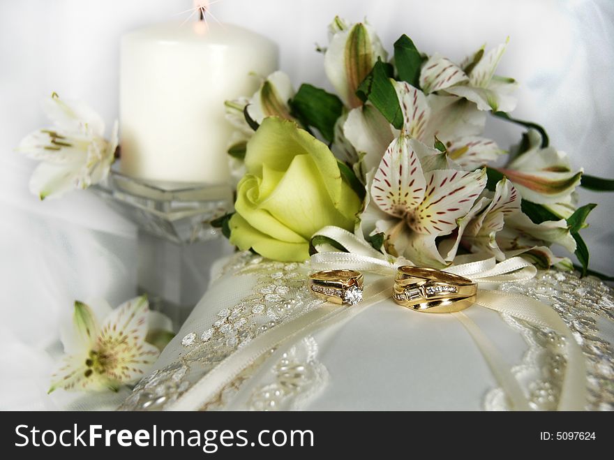 Wedding rings on a bridal pillow with bouquet and candle. Wedding rings on a bridal pillow with bouquet and candle.