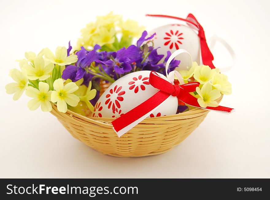 Easter eggs in basket with spring flowers on white background