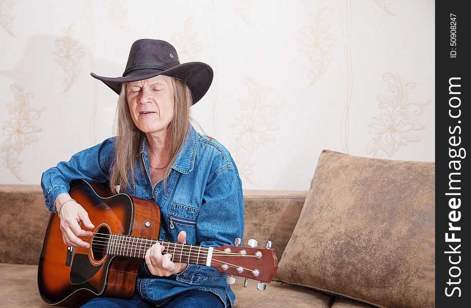 Middle-aged man in a hat plays guitar and sings at home