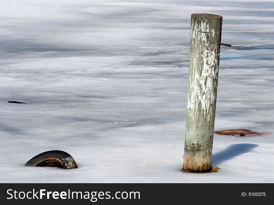 A post and tire frozen in the snow and ice at the Marina in late winter. A post and tire frozen in the snow and ice at the Marina in late winter.