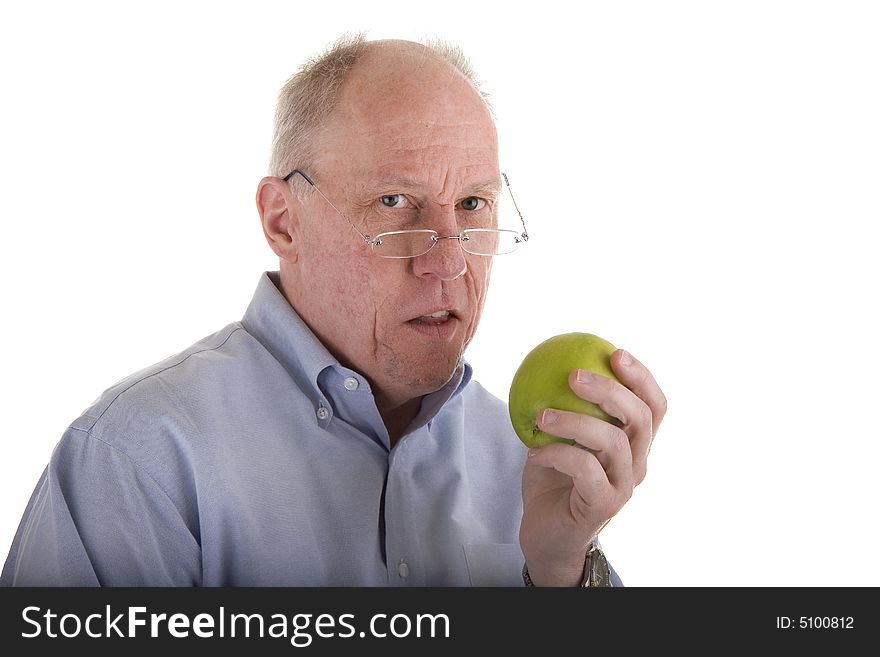 An older guy in a blue shirt and glasses holding an apple and looking at camera. An older guy in a blue shirt and glasses holding an apple and looking at camera