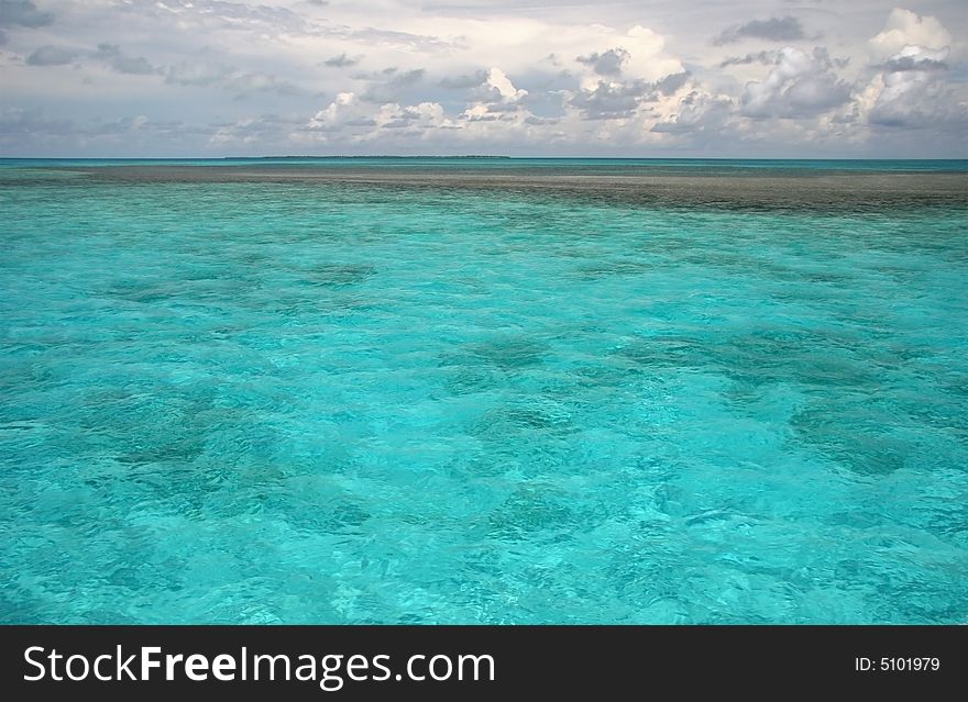 Line of black rocks in a shoal turquoise ocean water with summer resort in background. Barrier reef. Caribbean sea. Belize. Line of black rocks in a shoal turquoise ocean water with summer resort in background. Barrier reef. Caribbean sea. Belize