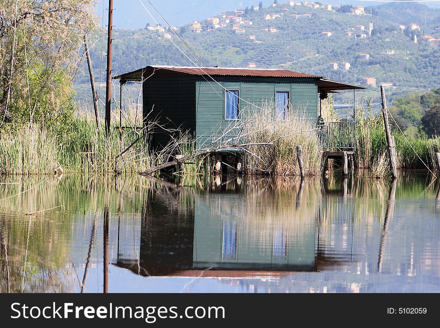 A fishing shed is reflected over the surface of a calm italian lake. A fishing shed is reflected over the surface of a calm italian lake