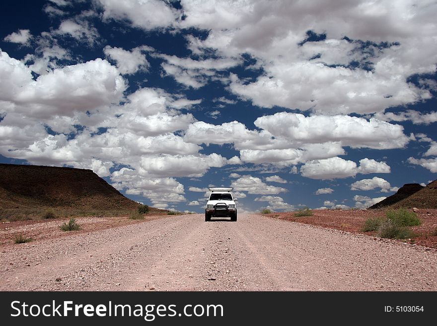 Beautiful cloudscape over the endless gravel road with a jeep driving through the desert. Namib desert. Namibia