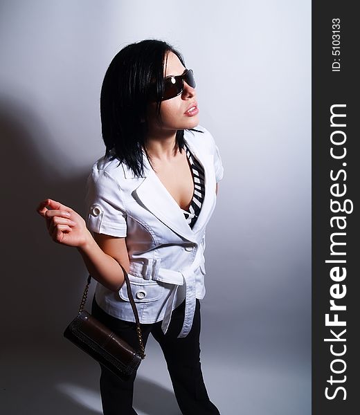 A high-key portrait about an attractive trendy lady with black hair who has a glamorous look. She is wearing sunglasses, black pants, a white coat and a stylish handbag. A high-key portrait about an attractive trendy lady with black hair who has a glamorous look. She is wearing sunglasses, black pants, a white coat and a stylish handbag.