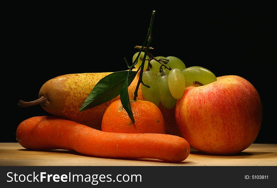 A pear, an apple, an orange, a carrot and a bunch of grapes on table. A pear, an apple, an orange, a carrot and a bunch of grapes on table