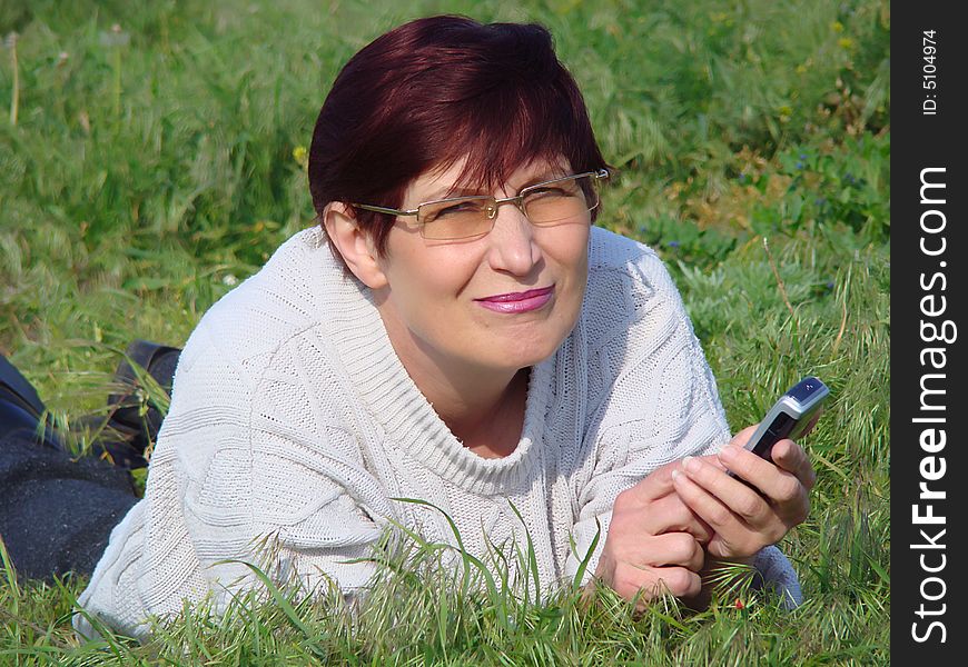 A happy business woman with a telephone rests on a grass. Beginning of tourist season. Mobile communication. A happy business woman with a telephone rests on a grass. Beginning of tourist season. Mobile communication.