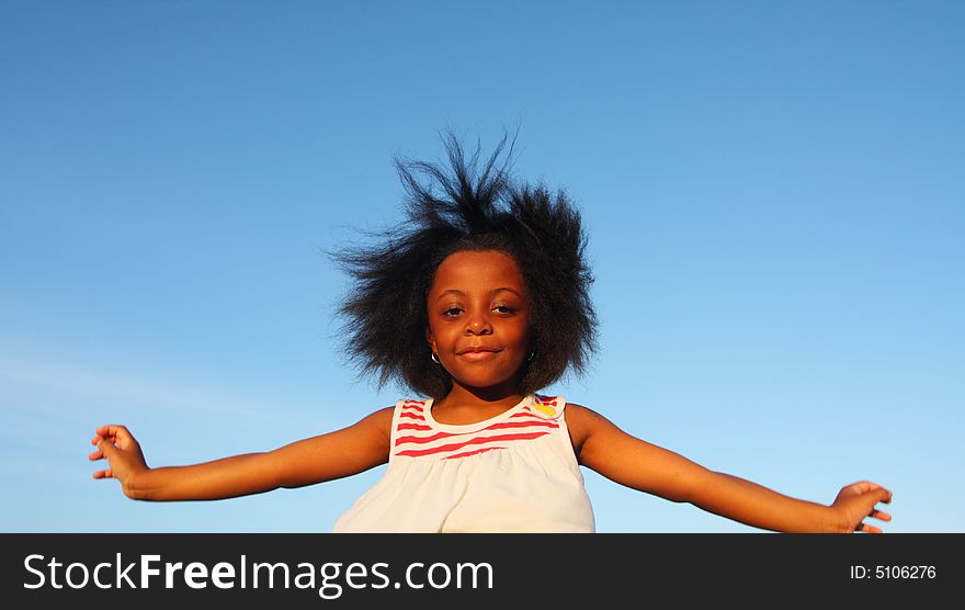 Young girl with her arms extended on blue sky background. Young girl with her arms extended on blue sky background.