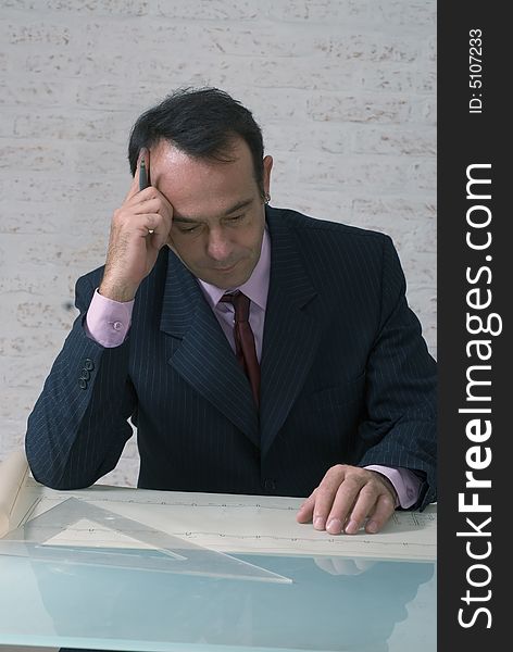 Latin american businessman reviewing plans and drawings on his office desk with his brow creased with concentration. Latin american businessman reviewing plans and drawings on his office desk with his brow creased with concentration