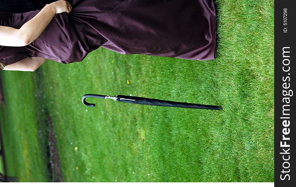 Black umbrella standing in grass, behind woman in purple formal dress. Black umbrella standing in grass, behind woman in purple formal dress