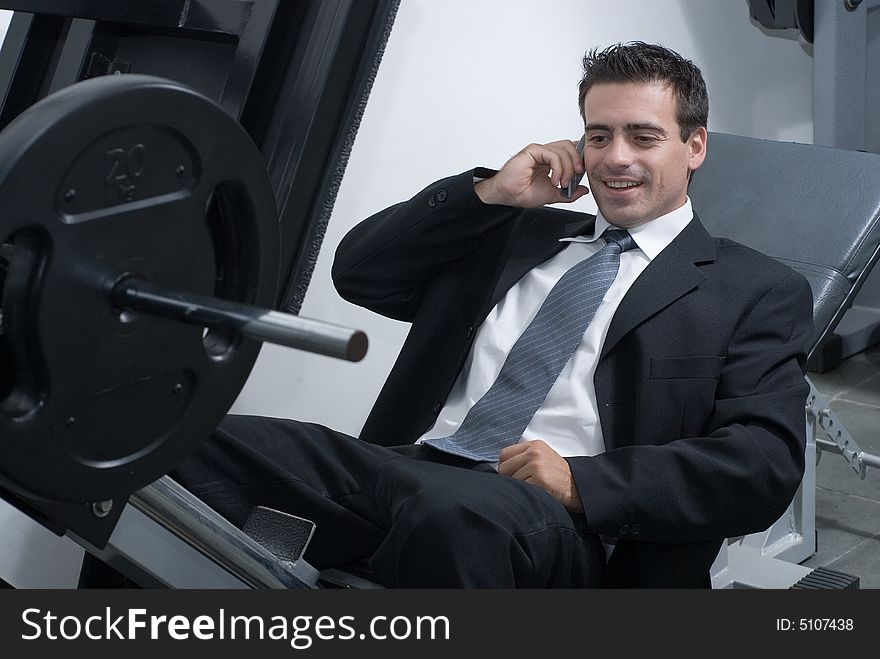 A shot of a businessman, in a suit, sitting on a weight machine talking on a cellphone. A shot of a businessman, in a suit, sitting on a weight machine talking on a cellphone.