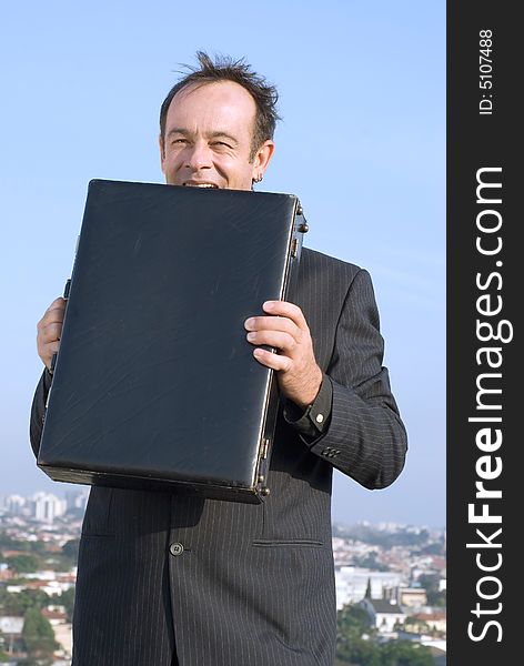 Latin american businessman standing on a city rooftop eating his briefcase in frustration. Latin american businessman standing on a city rooftop eating his briefcase in frustration