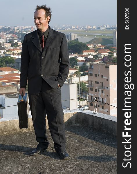 Businessman standing tall on a city rooftop while holding his briefcase. Businessman standing tall on a city rooftop while holding his briefcase