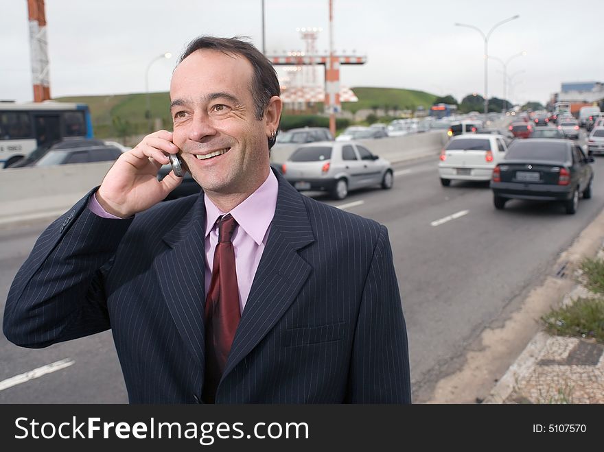 Businessman talking on his cellphone while standing on the side of a busy highway. Businessman talking on his cellphone while standing on the side of a busy highway