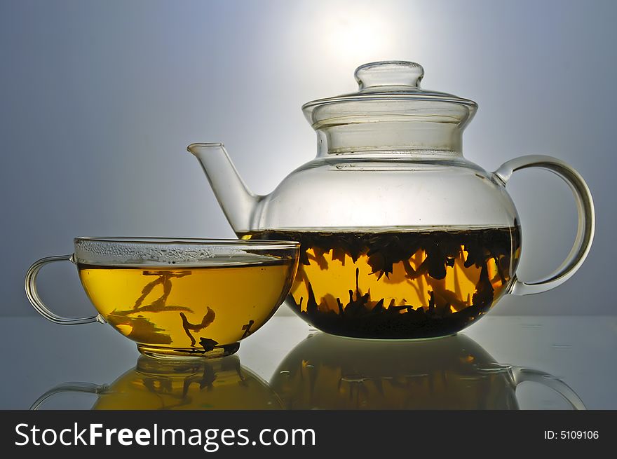 Glass teapot and cup with green tea on grey background. Glass teapot and cup with green tea on grey background