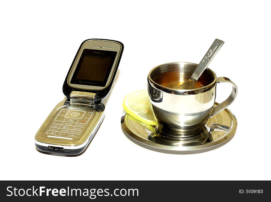 Metallic cup of tea with lemon on insulated white background with cellular telephones. Metallic cup of tea with lemon on insulated white background with cellular telephones