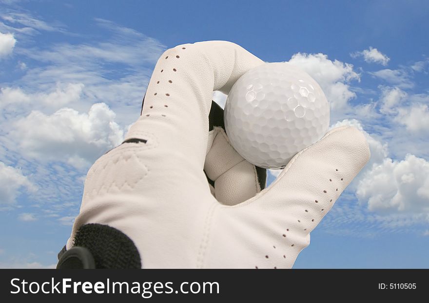 Hand holding a golf ball against the blue sky