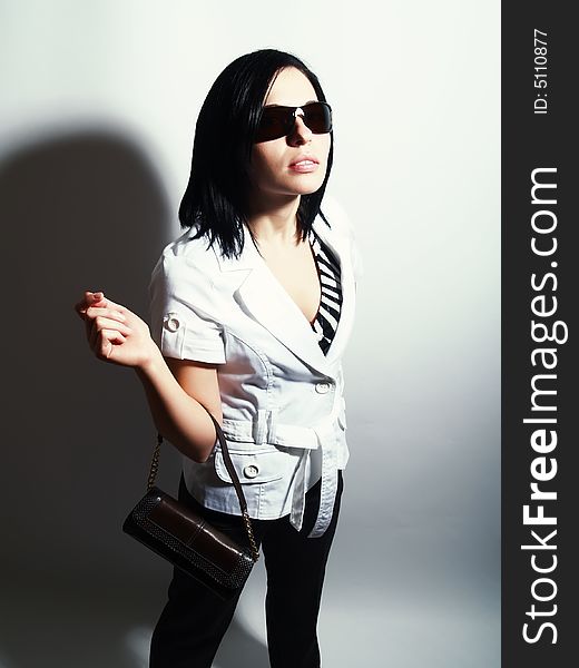 A high-key portrait about an attractive trendy lady with black hair who has a glamorous look. She is wearing sunglasses, black pants, a white coat and a stylish handbag. A high-key portrait about an attractive trendy lady with black hair who has a glamorous look. She is wearing sunglasses, black pants, a white coat and a stylish handbag.